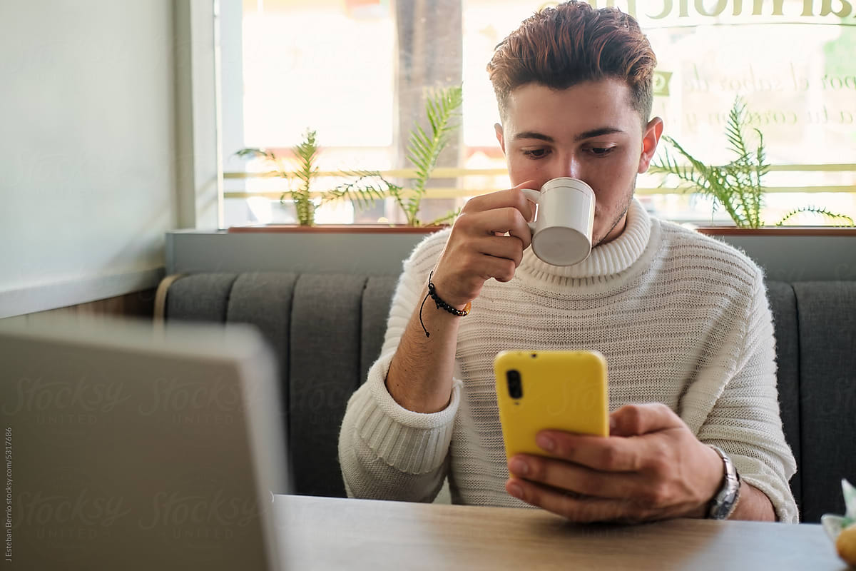 Young man enjoying a cup of coffee while looking at his phone