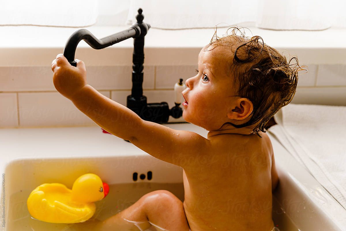 Baby playing with toy duck in the kitchen sink