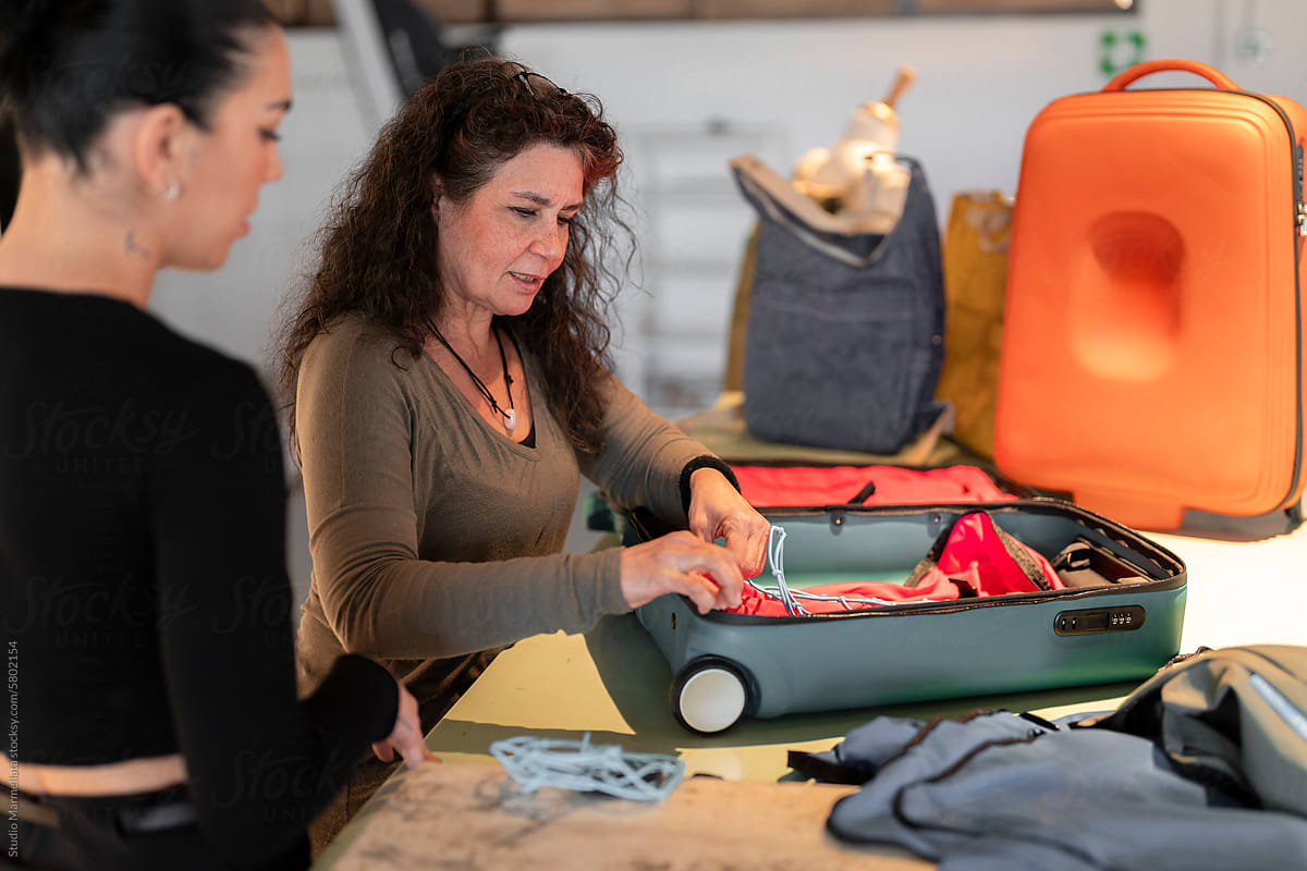 women colleagues discussing and adding inside net in suitcase