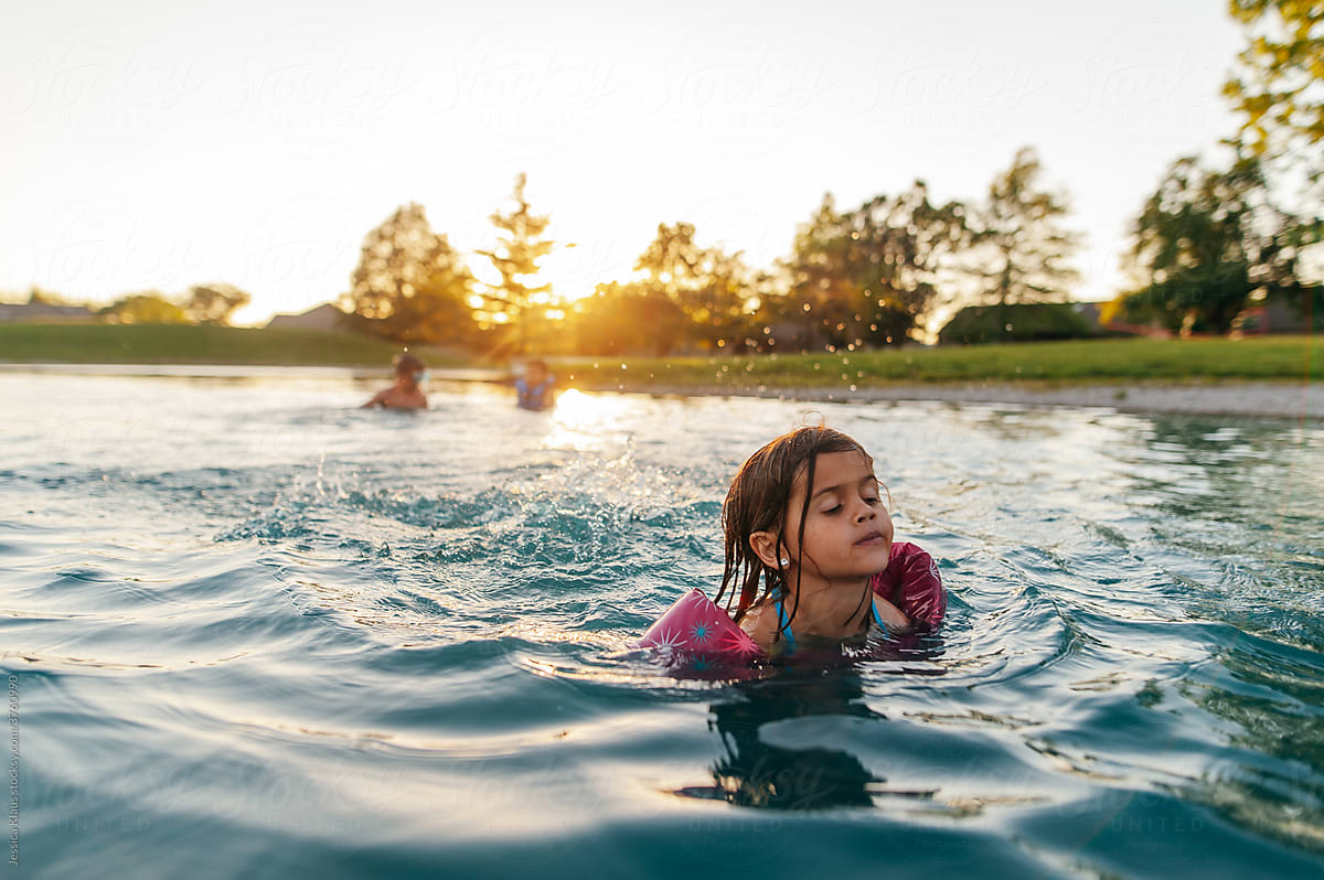 Child swimming in pond at sunset.
