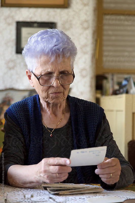 Senior woman sitting at the table in her living room, looking at the old family photo