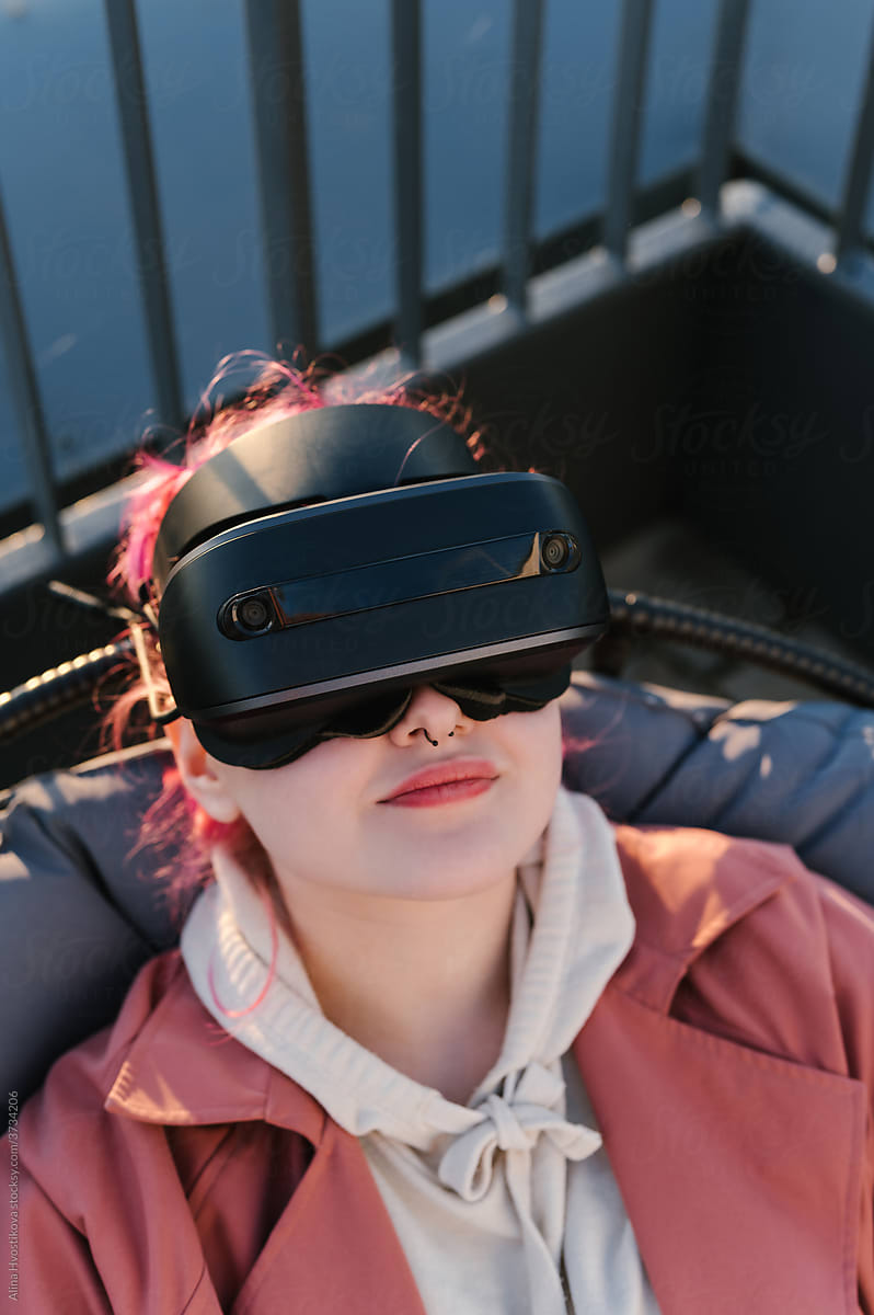 Young female in VR glasses resting on balcony