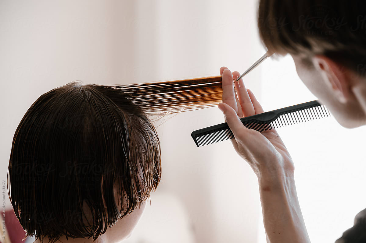 Crop hairstylist cutting hair of woman