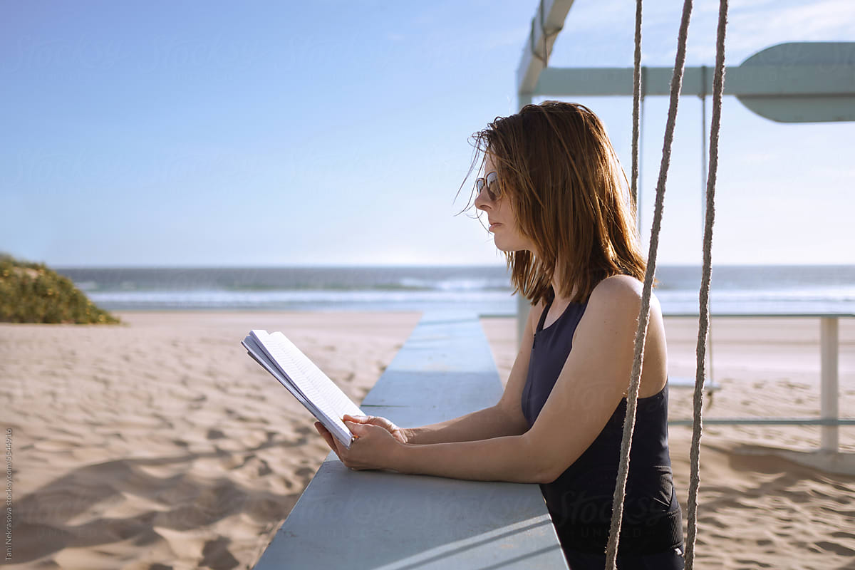 A young woman on the ocean reading a book