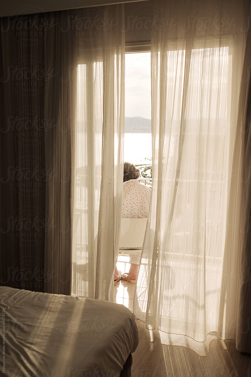 Senior woman on a balcony among curtains