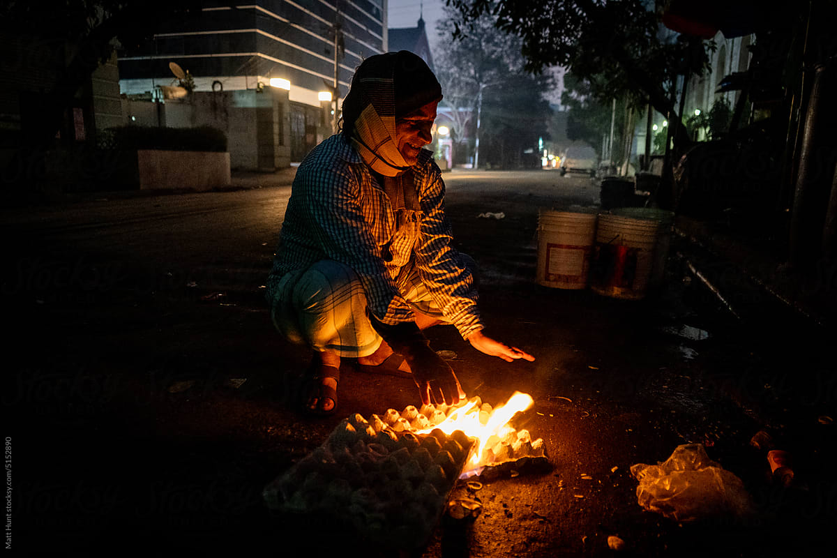 A man smiles while keeping warm over a fire on the street in India