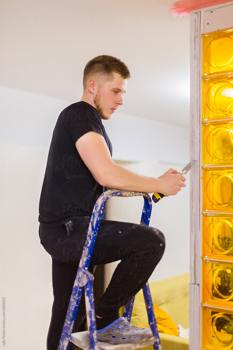 A man  makes repairs installing a wall of yellow blocks