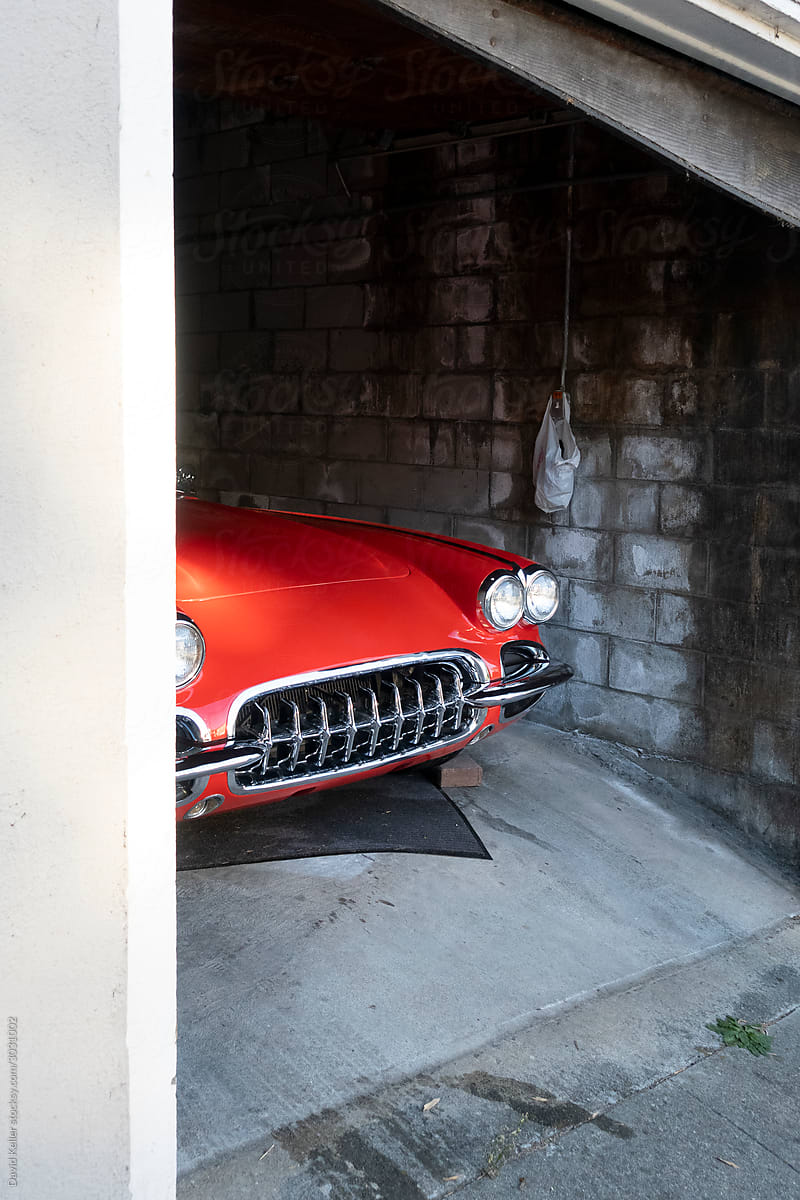 A vintage red car peeking out of a small garage