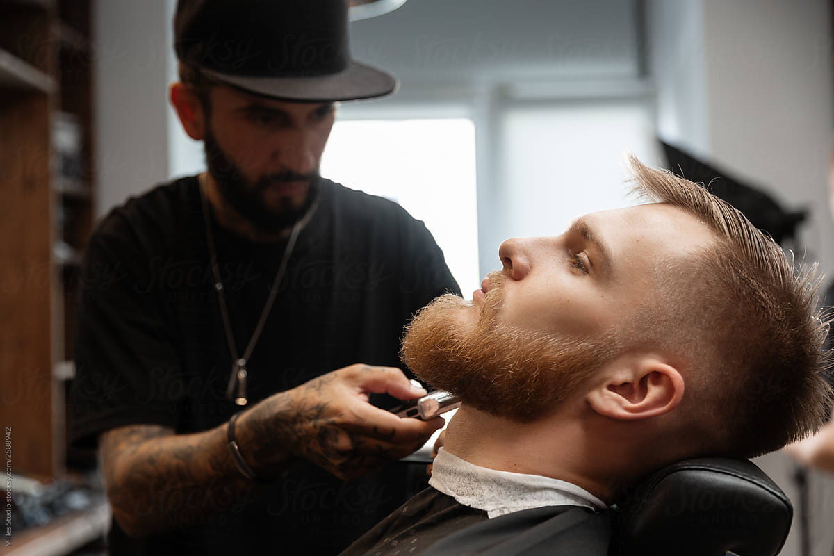 Focused barber shaving beard of young man