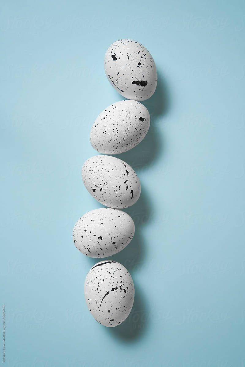 Speckled Easter colored eggs lined up on a pastel blue background.