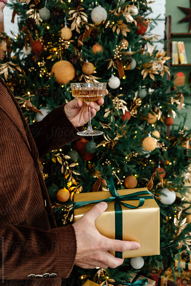 Man holding gift and glass of champagne near Christmas tree