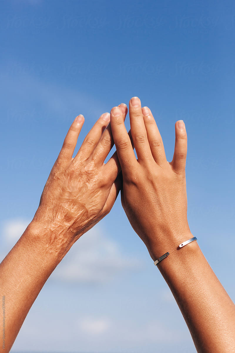 Closeup of young woman tanned hands up on blue summer sky and sea background.