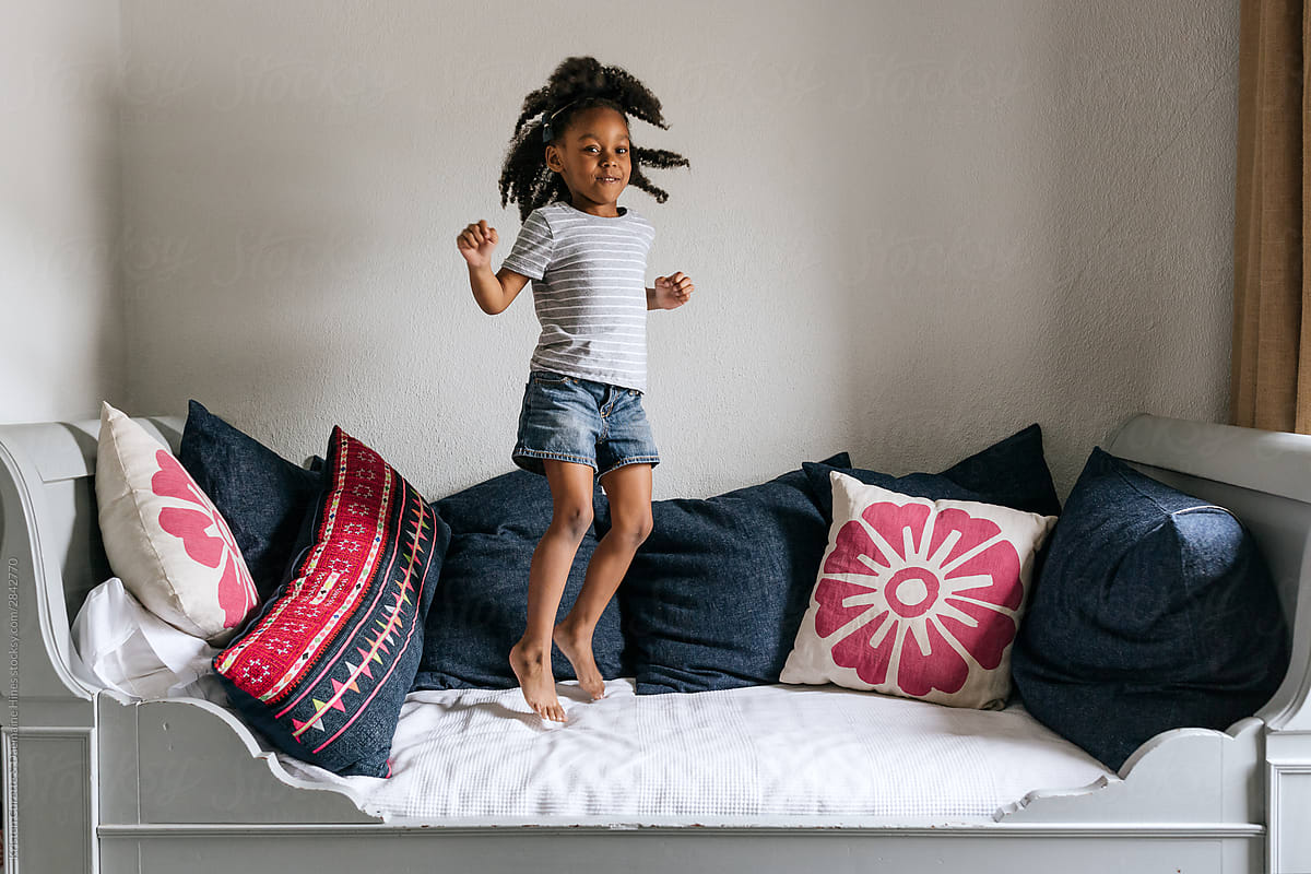 A little girl jumping up & down on a bed.