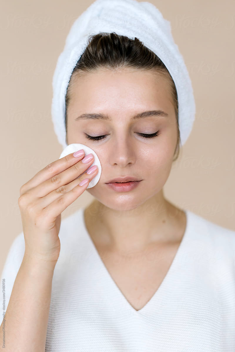 Young woman wiping face skin with cotton pad