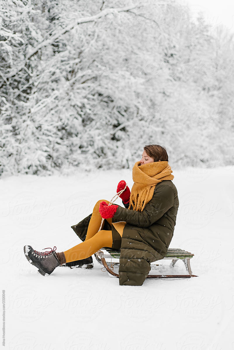 Young woman sitting on sledge in winter forest