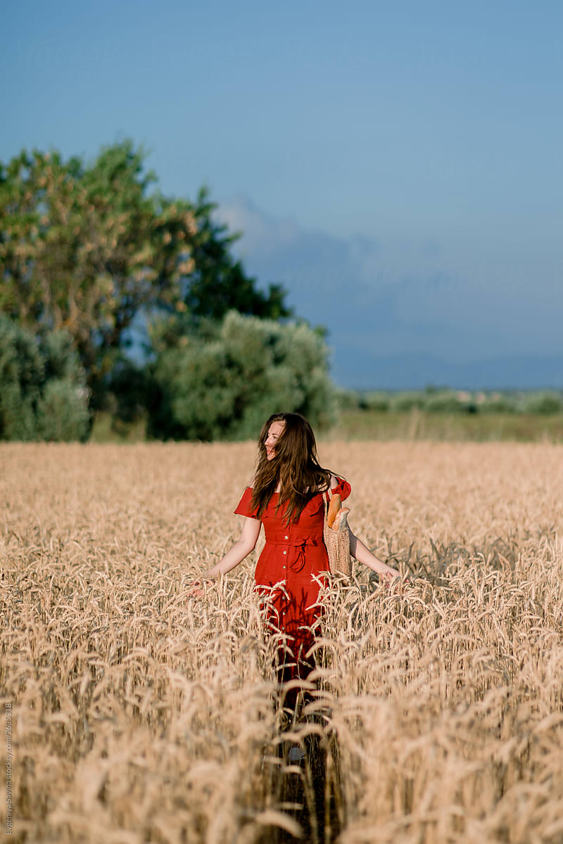 A dark-haired girl in a red dress standing in rye fields in the golden evening light