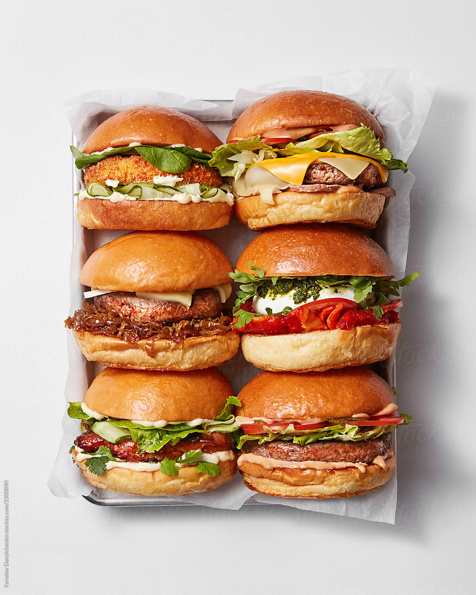 Set of a variety of fresh burgers with greens, vegetables, cheese and meat in a paper box on a gray background with copy space. Dinner. Top view