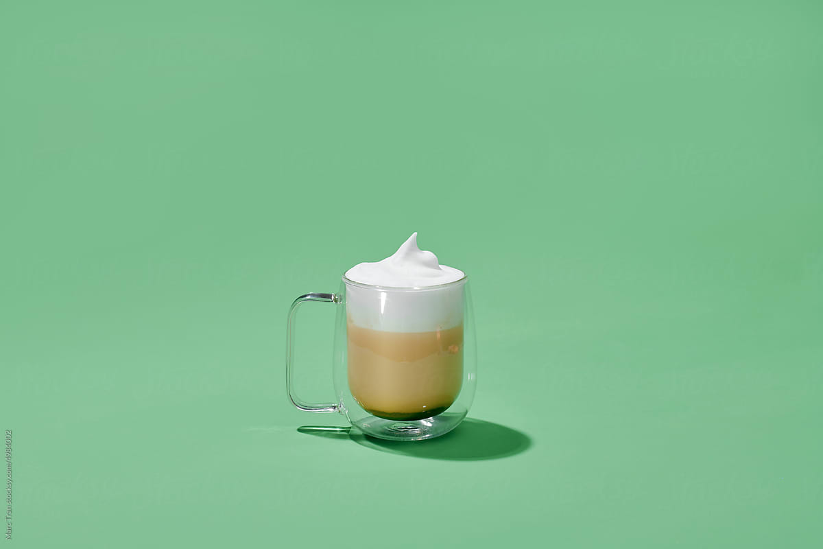 Cappuccino in glass cup with double walls isolated on green background