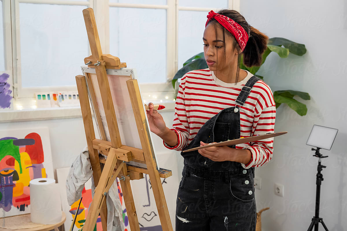 Black woman painting on easel in art studio