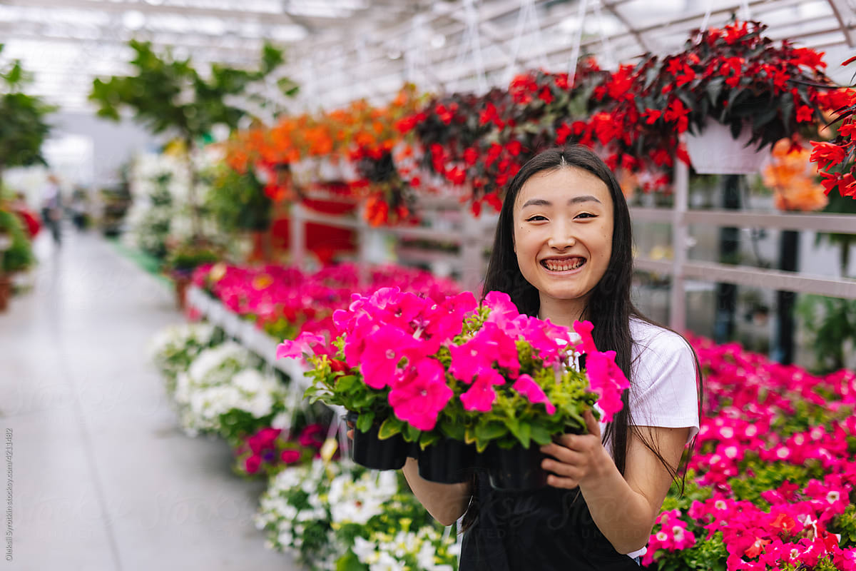 Asian girl smiling and showing flowers in pot at camera