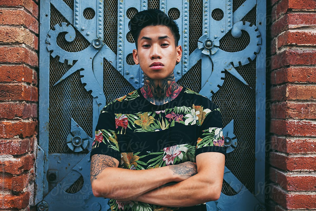 Portrait of a young asian tattooed man standing in front of a blue door.