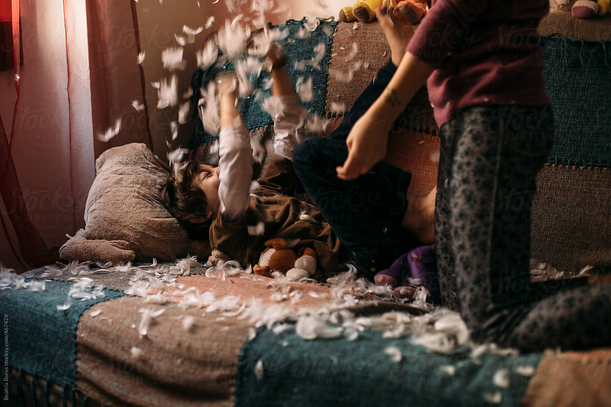 Sibling's pillow fight on a sofa, feathers flying all over