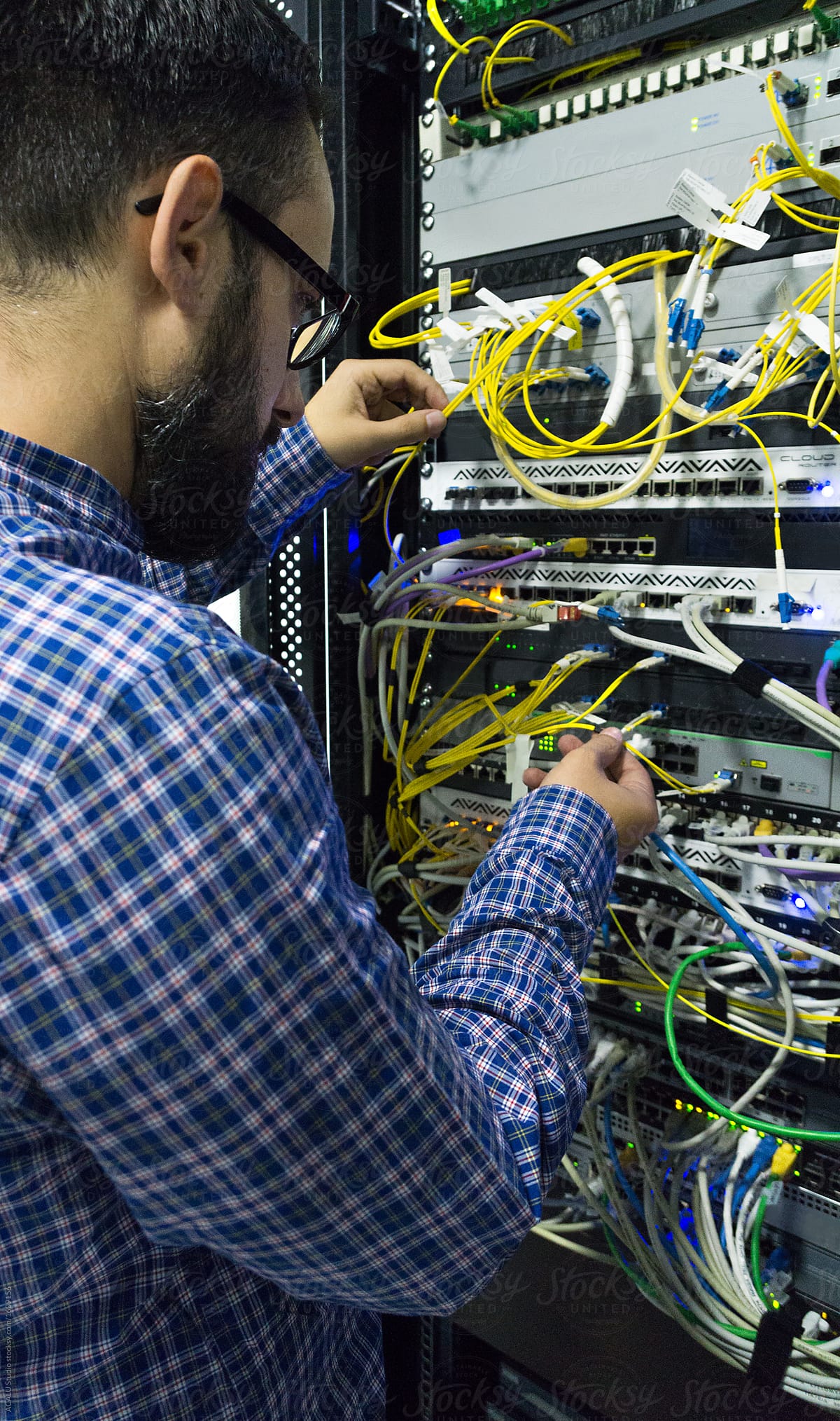 Technician reaches up into a tangle of network cables a rack of