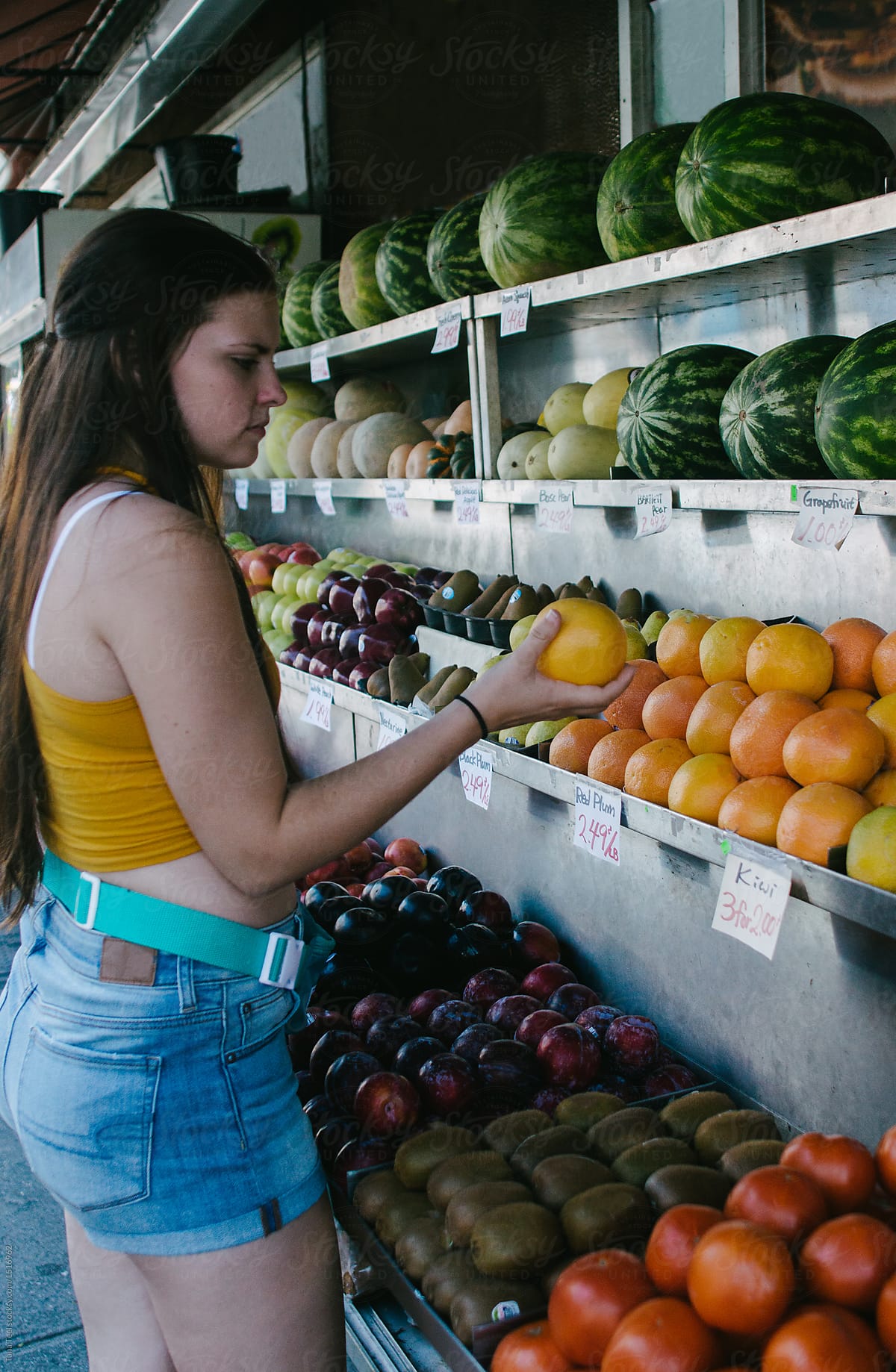 young woman looking at fresh fruit at an open street store