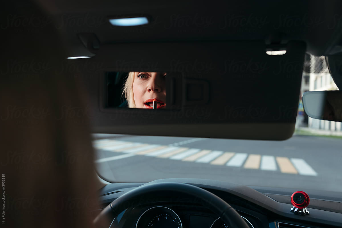 A middle-aged woman does makeup while sitting in a car.