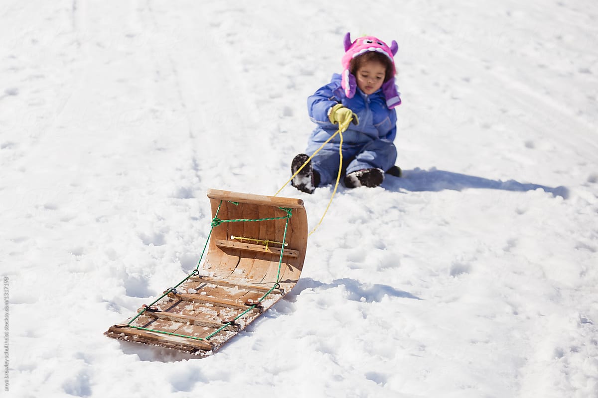 Toddler child trying to pull a toboggan up a snowy hill