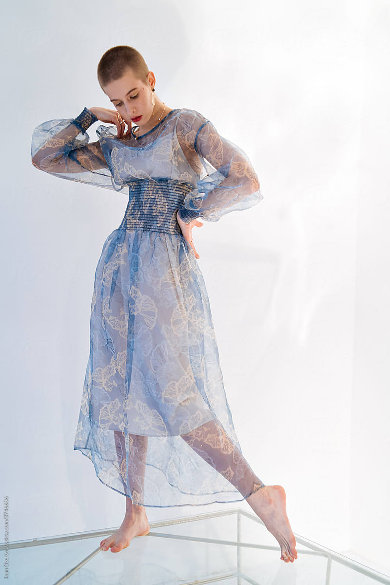 bald barefoot model in a transparent light dress posing in the studio