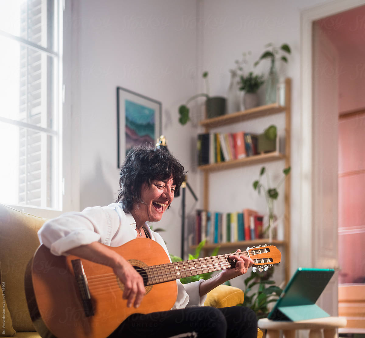 Cheerful mature woman learning to play guitar with tablet at home