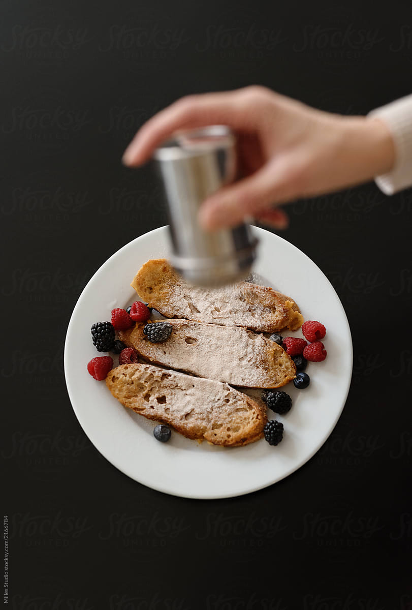 Crop woman sprinkling toasts with sugar powder