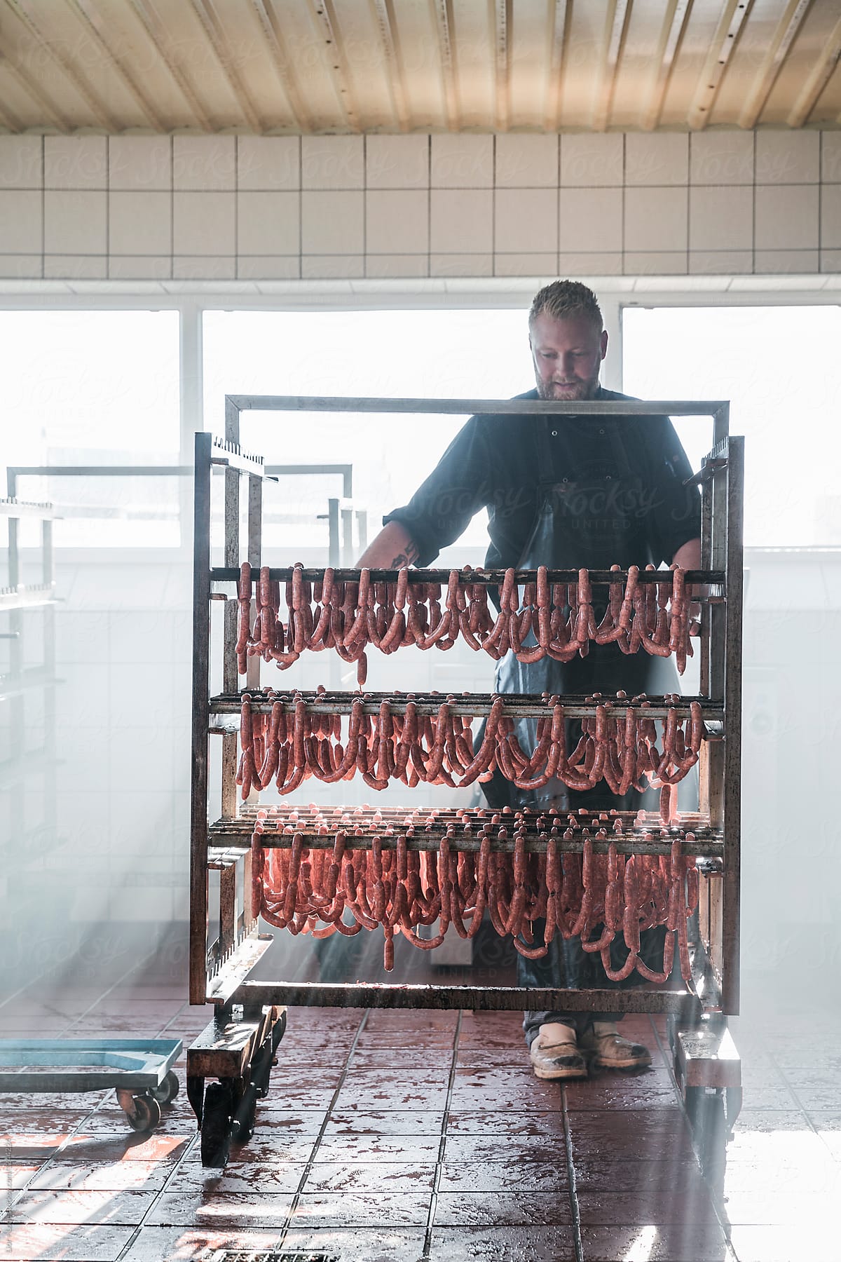 Butcher hanging fresh sausages on a smoking rack