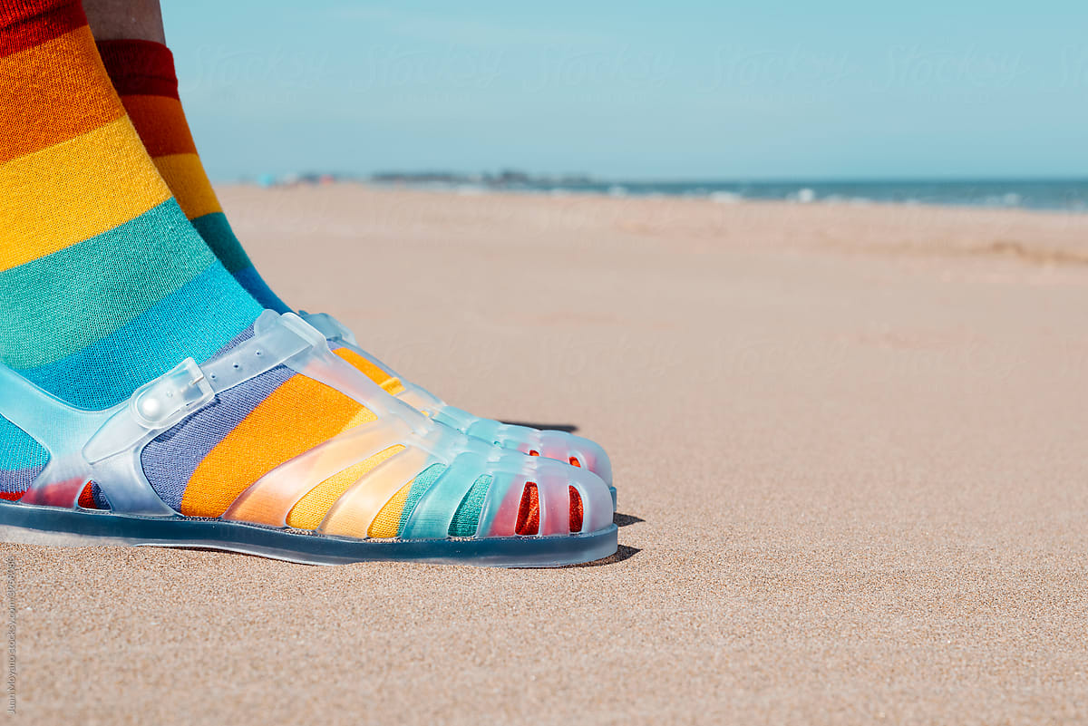 on the sand wearing rainbow patterned socks and sandals