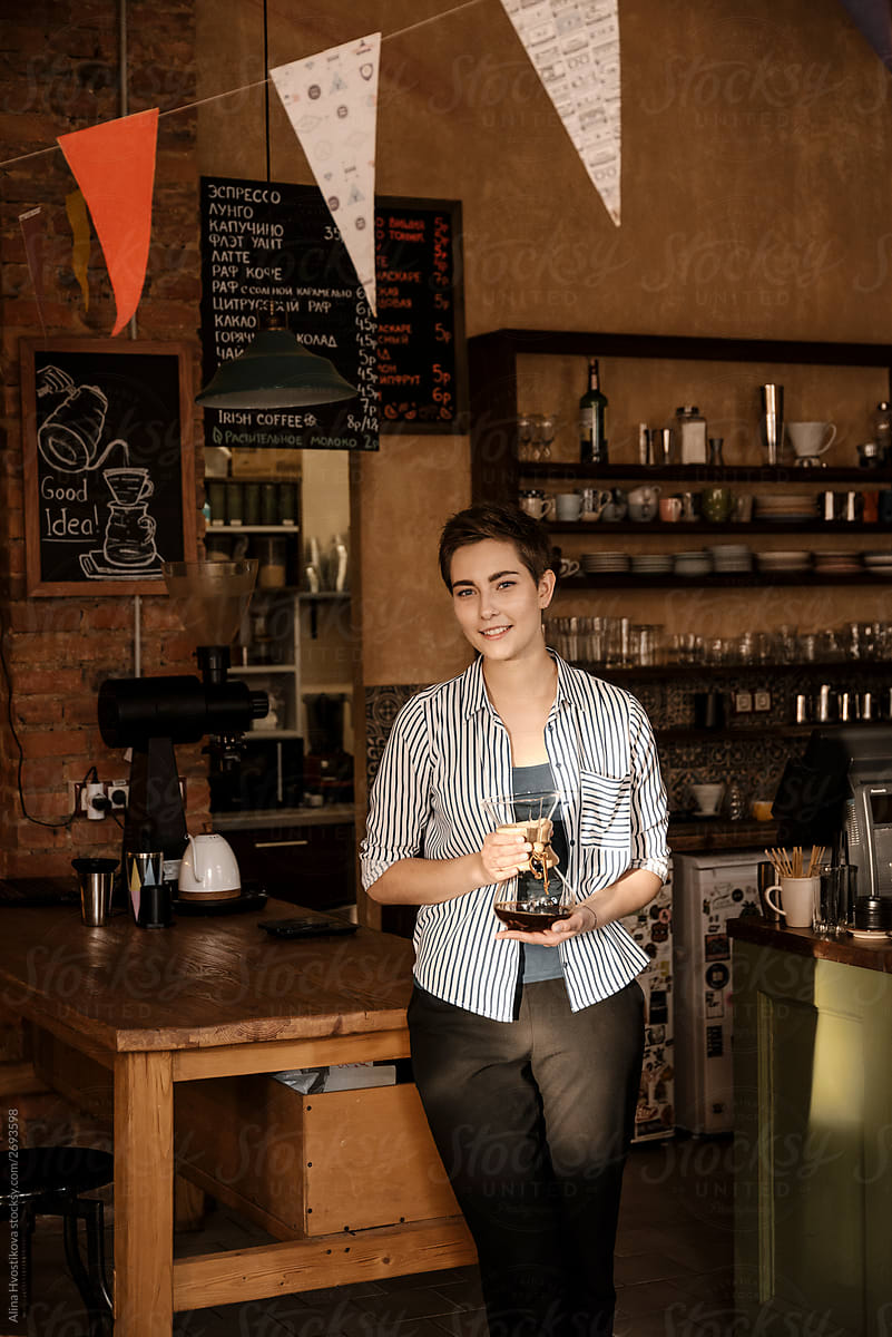 Barista girl holding glasses pot with coffee and smiling.
