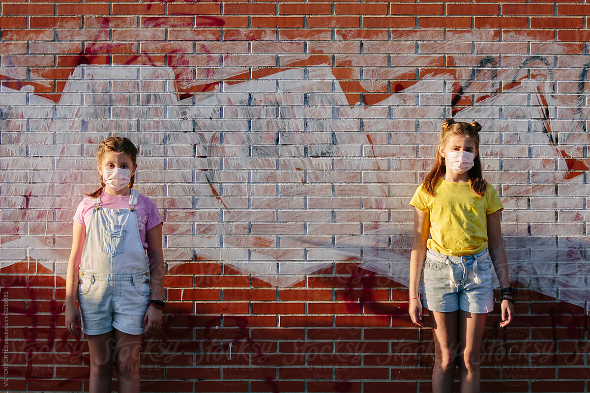 Girls standing besides a brick wall with masks