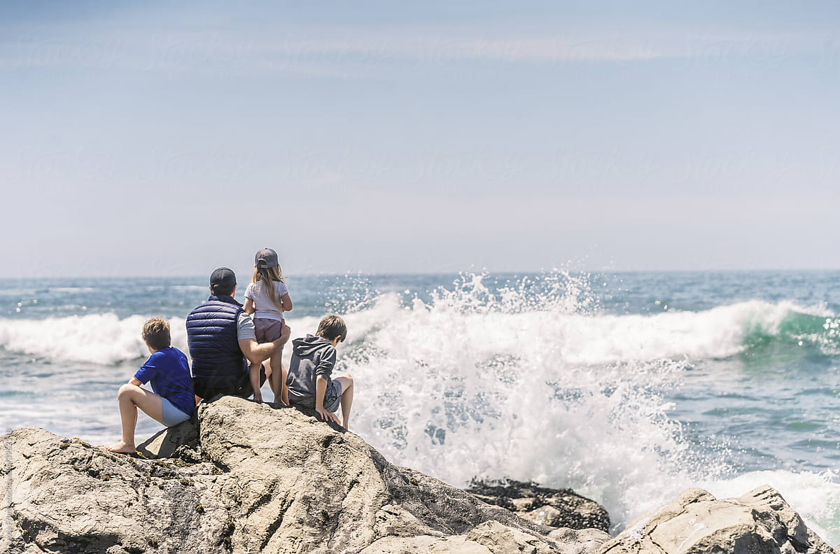 family sitting on rocky coastline with waves