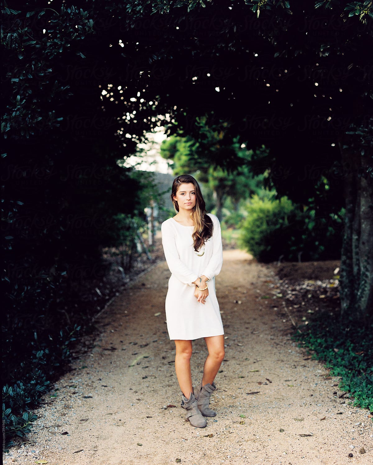 Beautiful girl in a sweater dress standing outside on a gravel walkway