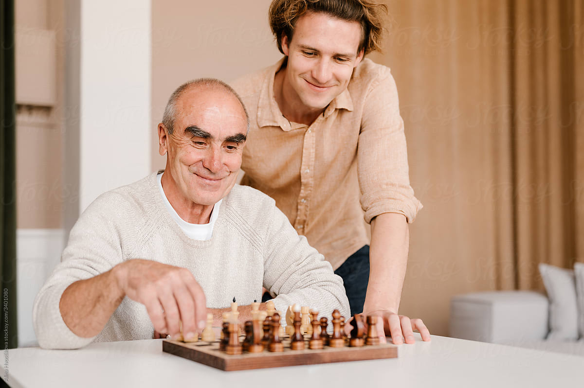 Happy senior man with son playing chess at home