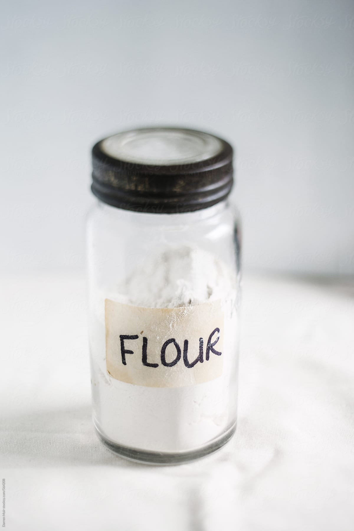 Glass jar of flour on off white background. Selective focus on the label.