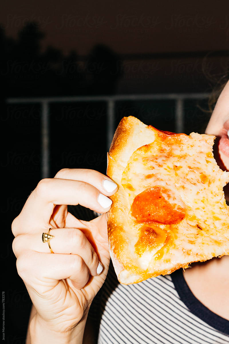 young female holding and eating pizza looking away from camera