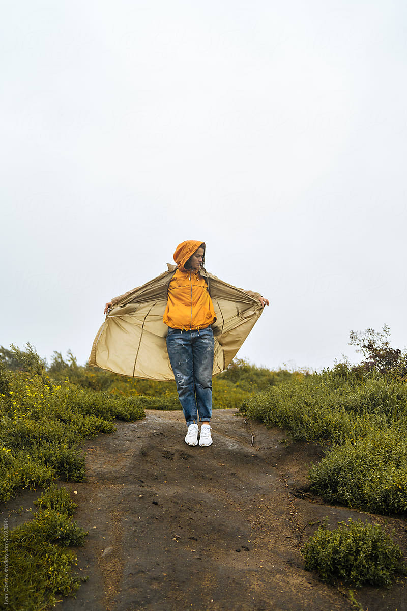 A woman in a raincoat stands on a hill,