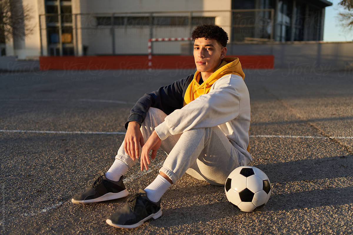 Serious man with soccer ball sitting on sports ground
