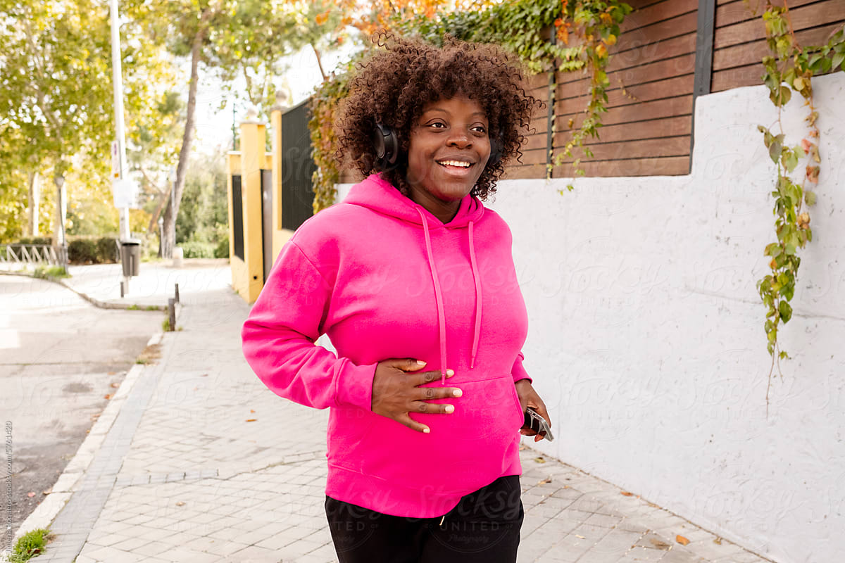 Happy Pregnant woman jogging on the street with headphones