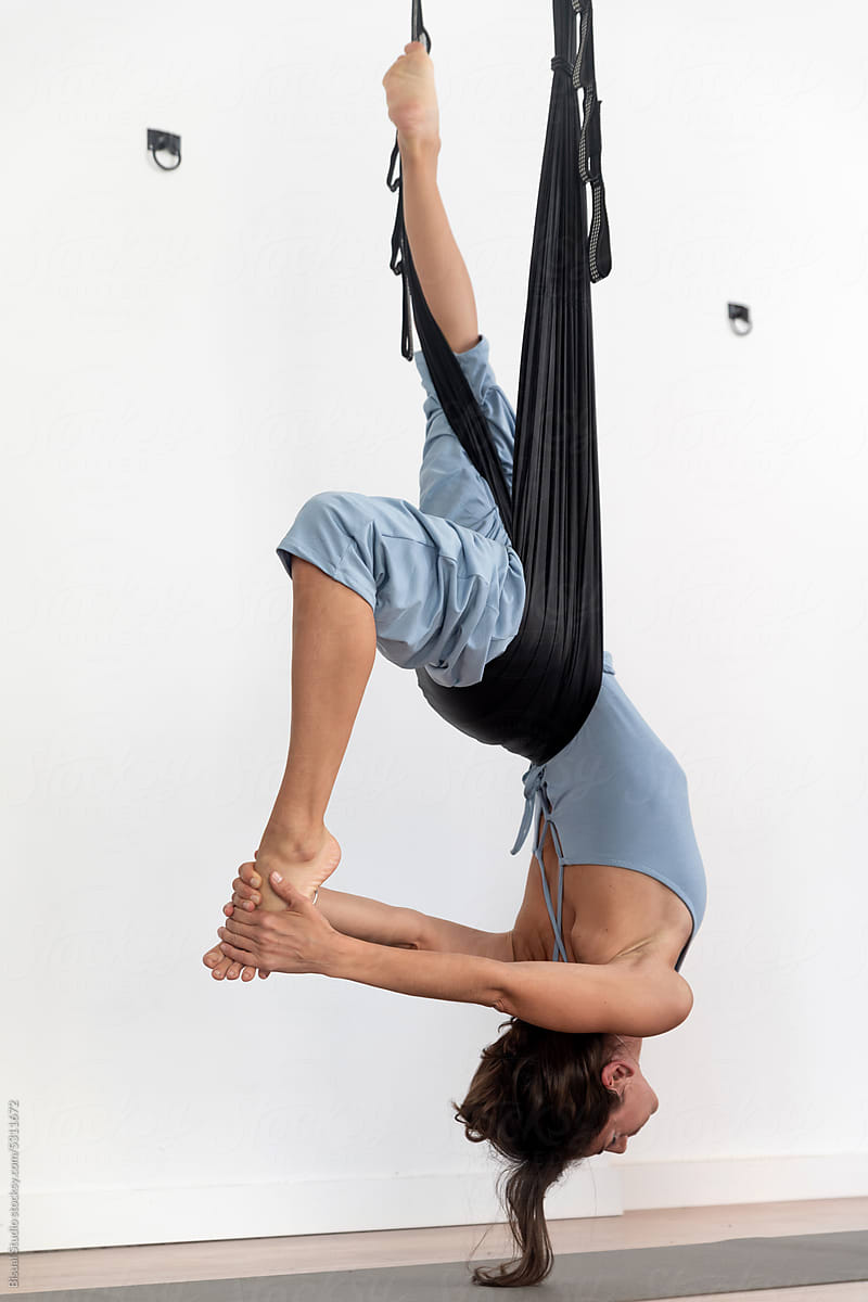 Flexible woman doing aerial yoga exercise on ropes