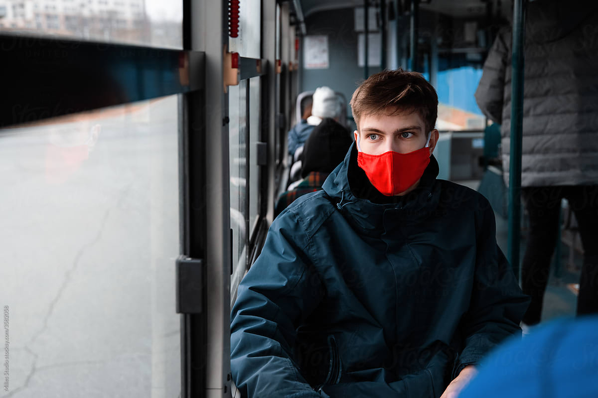 Young man in mask sitting near window in bus