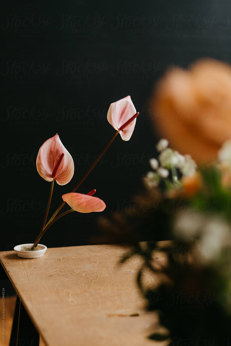 High end artistic floral arrangement in studio on wooden table against black backdrop.