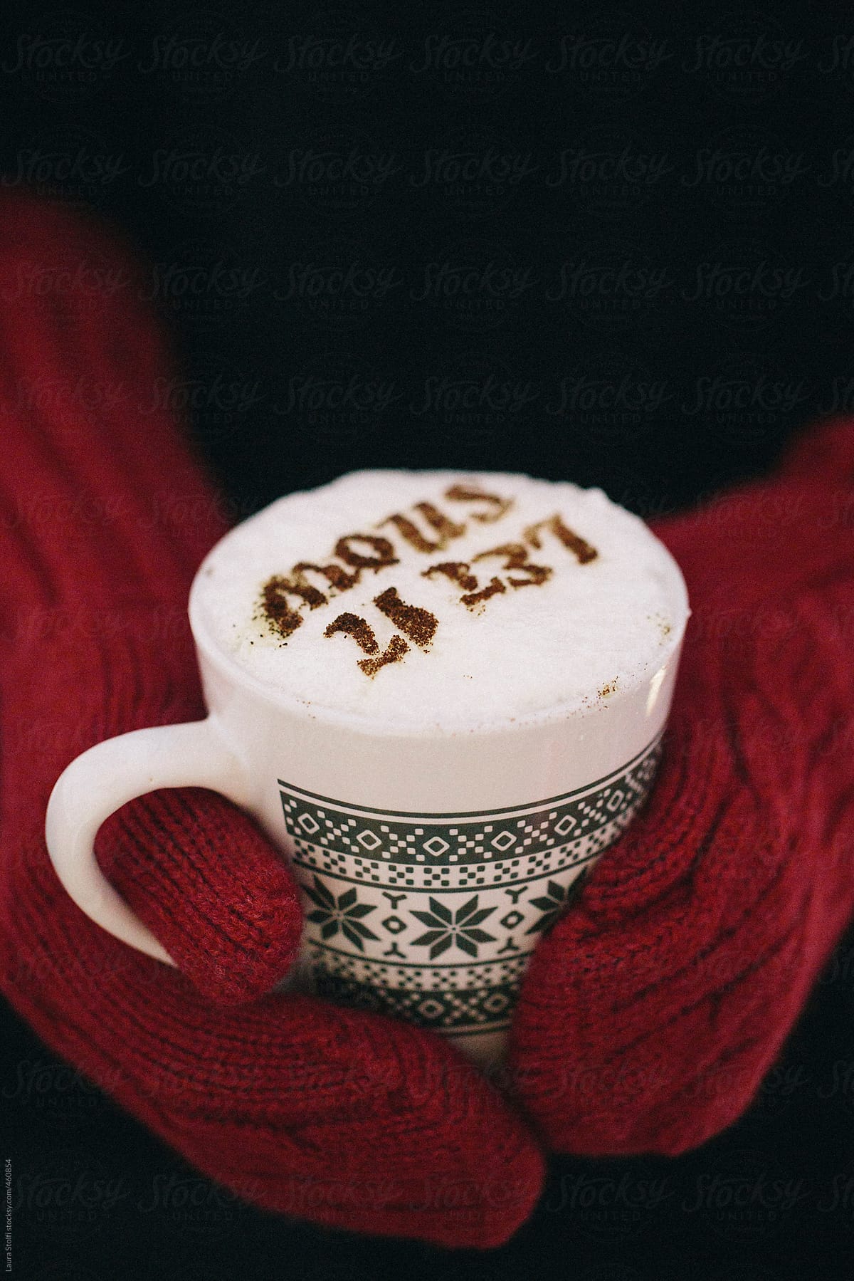 Hands wearing red woolen mittens and holding a mug of chocolate with words Let it snow on foam