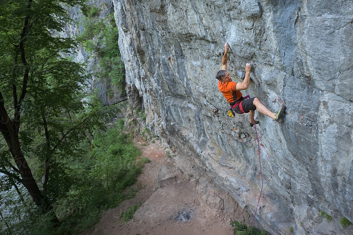 Male adult rock climbing on steep wall using safety rope